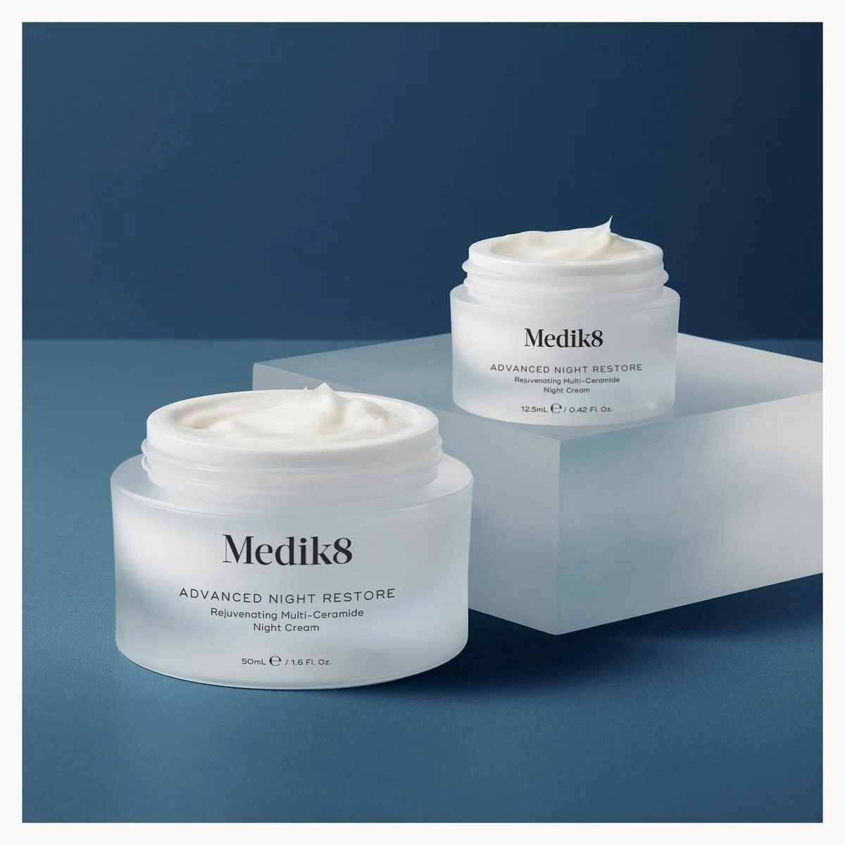 Two jars of Medik8 Advanced Night Restore cream on a blue background
