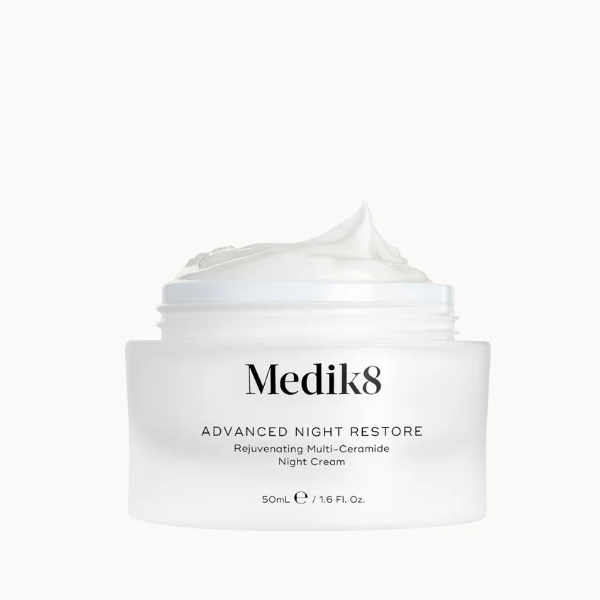 A white jar of Medik8 Advanced Night Restore Reluminating Multi-Ceramide Night Cream with a dollop of cream on top, set against a solid white background.