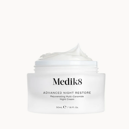 A white jar of Medik8 Advanced Night Restore Reluminating Multi-Ceramide Night Cream with a dollop of cream on top, set against a solid white background.
