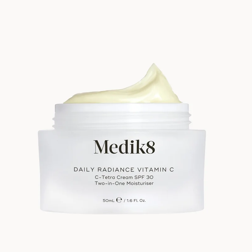 A white jar of Medik8 Daily Radiance Vitamin C C-Tetra Cream SPF 30 Two-in-One Moisturizer with a swirl of pale yellow cream on top, set against a solid off-white background.