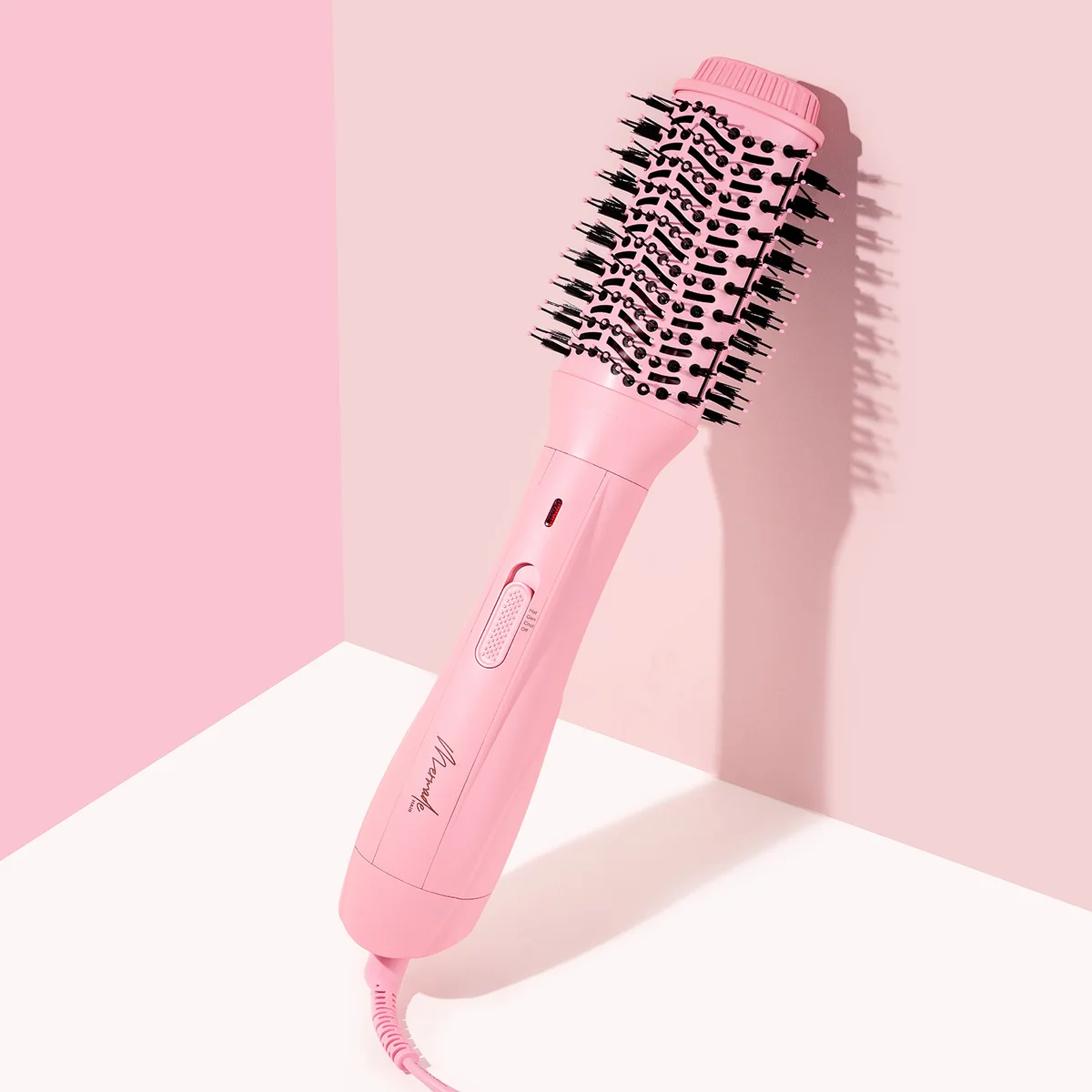 Pink round hairbrush with black bristles, leaning against a pink wall on a white surface.