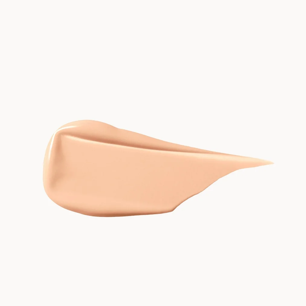 A smooth, swirled smear of light peach-beige liquid foundation or cream makeup on a solid white background.