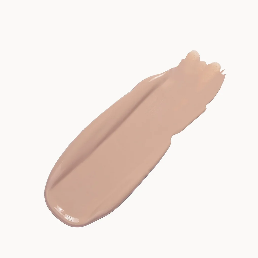 A smooth, diagonal swipe of liquid foundation or concealer in a warm, light beige shade against a clean, off-white background.