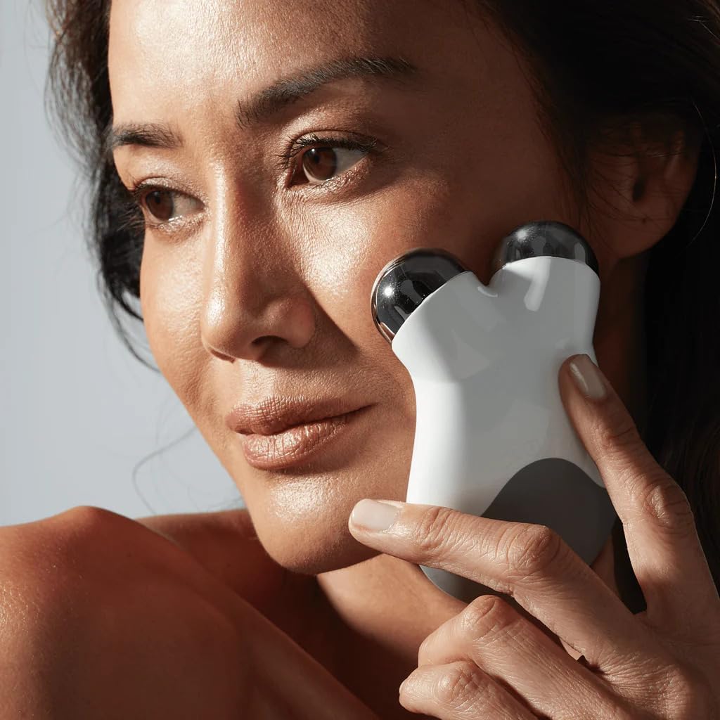 Woman using a white facial device on her face against a neutral background