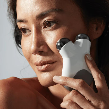 Woman using a white facial device on her face against a neutral background