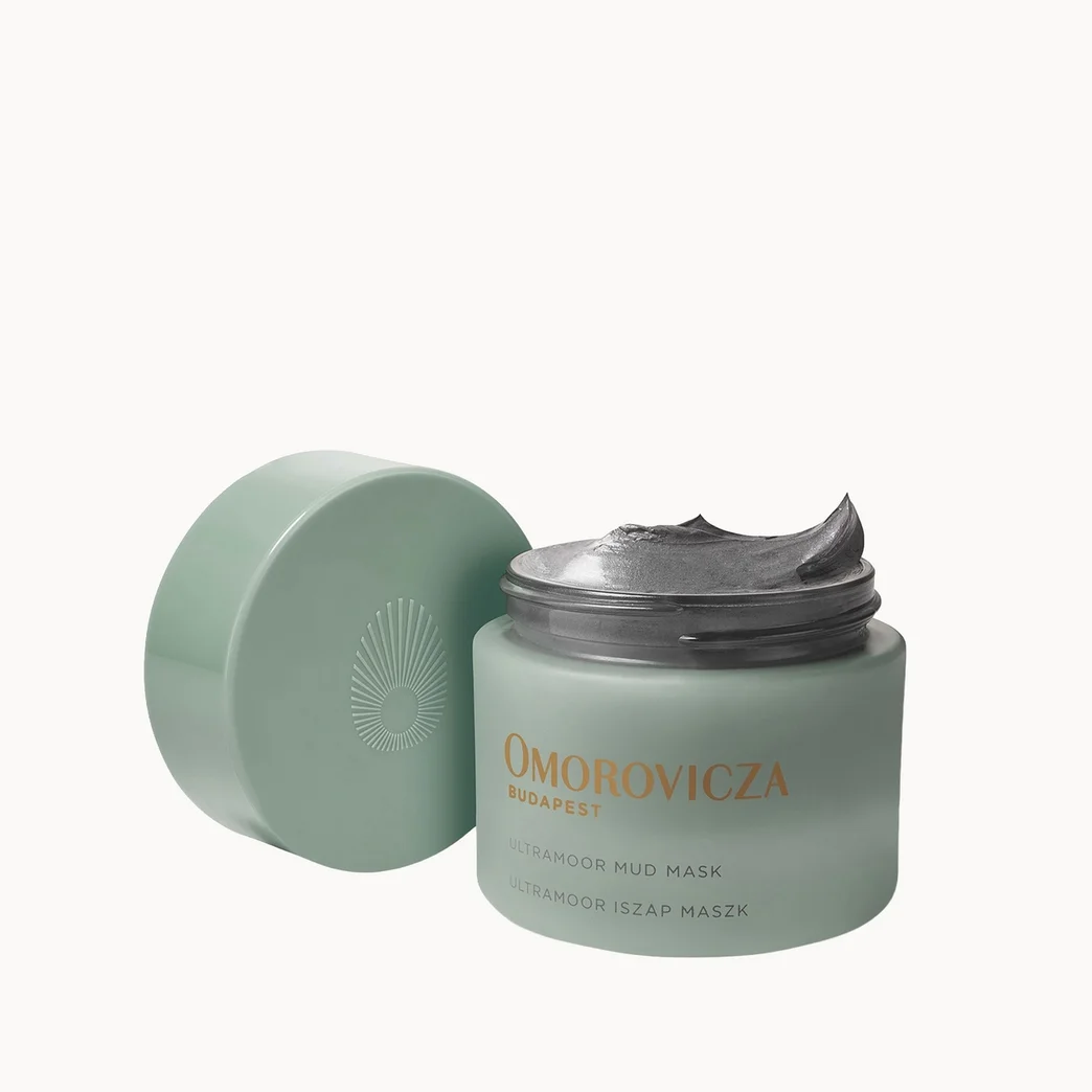 A light sage green cosmetic jar of Omobovicza Hyaluveil Hydration Sugar Mask with its lid off, showing a silver-toned cream inside, on a solid white background.