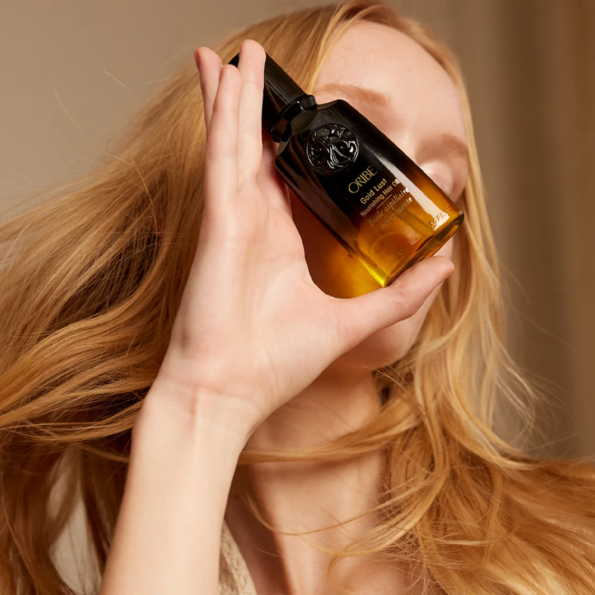 Person holding a black and gold perfume bottle with a blurred background