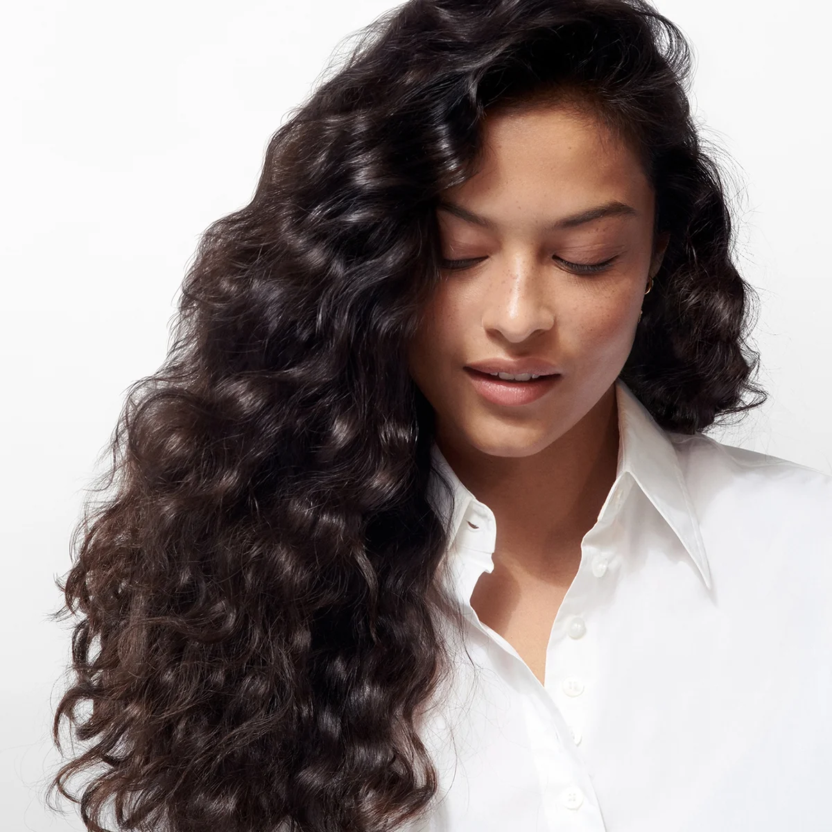 Woman with long, wavy hair wearing a white shirt on a light background