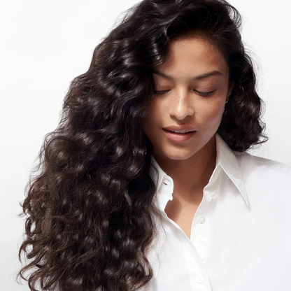 Woman with long, wavy hair wearing a white shirt on a light background