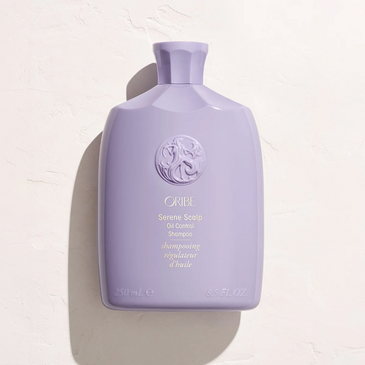 A lavender purple bottle of Oribe Serene Scalp Oil Control Shampoo, photographed from a high angle against a textured off-white background with a soft shadow.