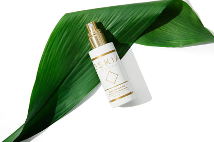 Skincare bottle with gold cap on a green leaf against a white background