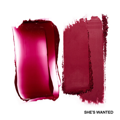 Close-up of a bright pink lipstick swatch with 'SHE'S WANTED' text on a white background