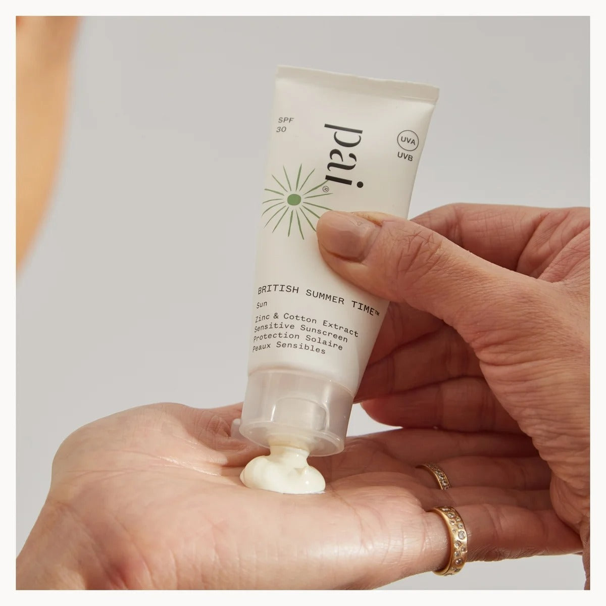 Hand holding a tube of Pai skincare product with cream on the palm against a neutral background