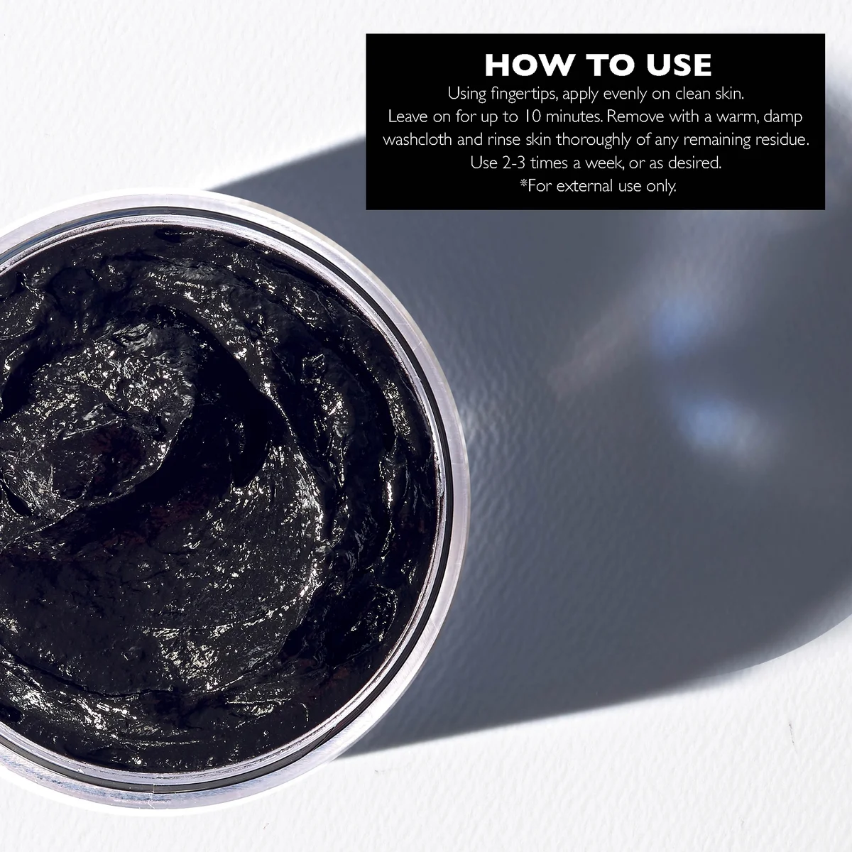 Black charcoal face mask in a container with usage instructions on a white background