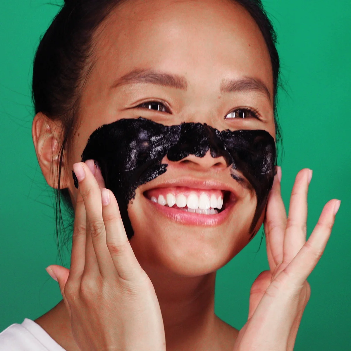 Woman applying black facial mask on a green background