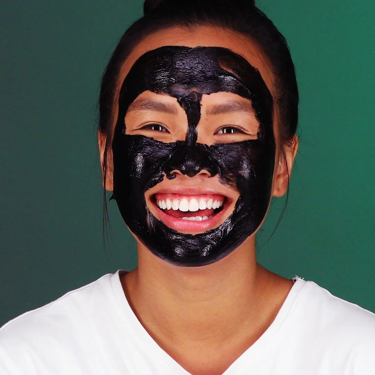 A smiling woman with a black bud skin mask applied a green background