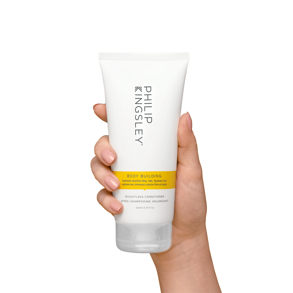 Hand holding a tube of Philip Kingsley Body Building product on a white background