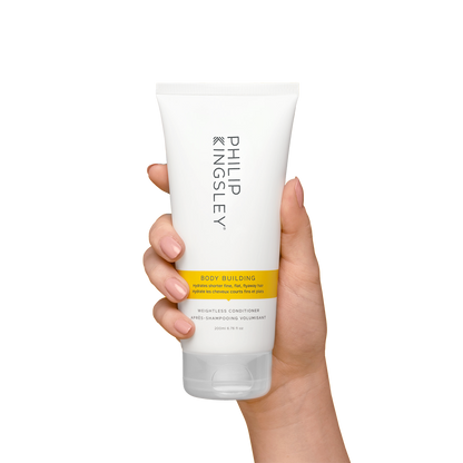 Hand holding a tube of Philip Kingsley Body Building product on a white background