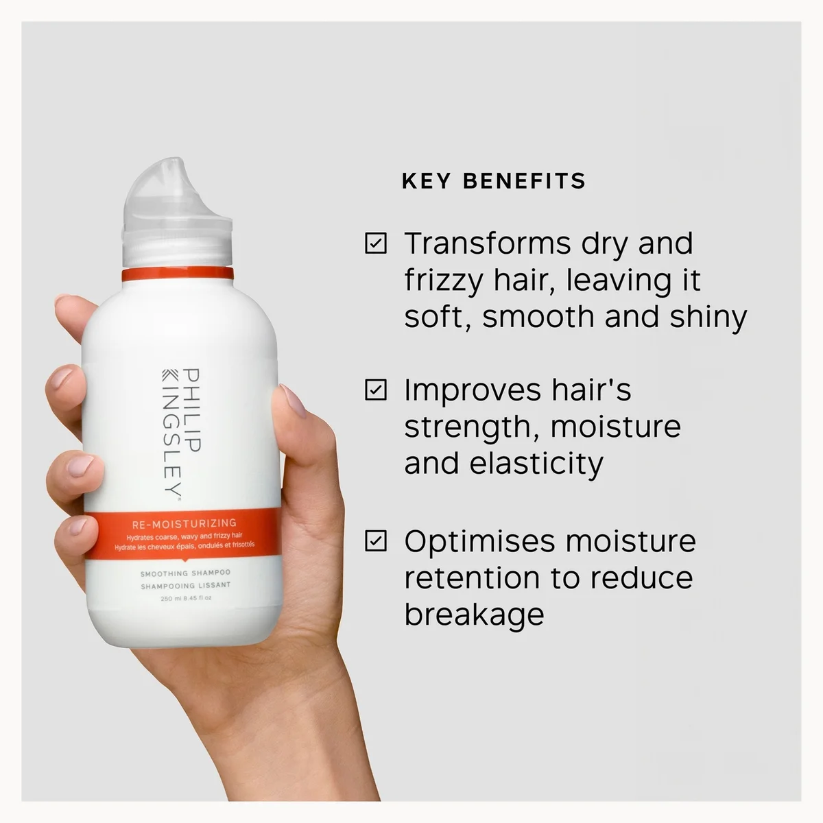 Hand holding a bottle of Philip Kingsley hair product with key benefits listed on a gray background