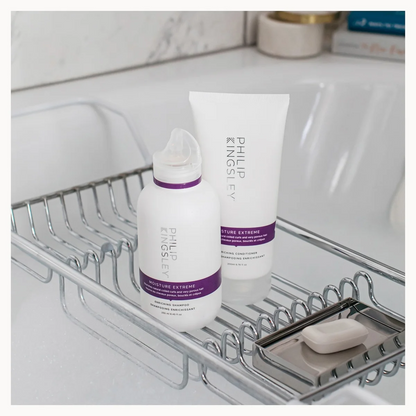Philips Haircare hair extension care products, including a white bottle and tube with purple bands, displayed on a chrome wire bathroom sink caddy.