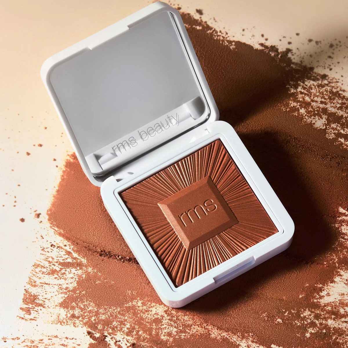 Open RMS Beauty compact with brown powder on a beige background