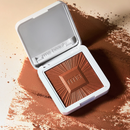 Open RMS Beauty compact with brown powder on a beige background