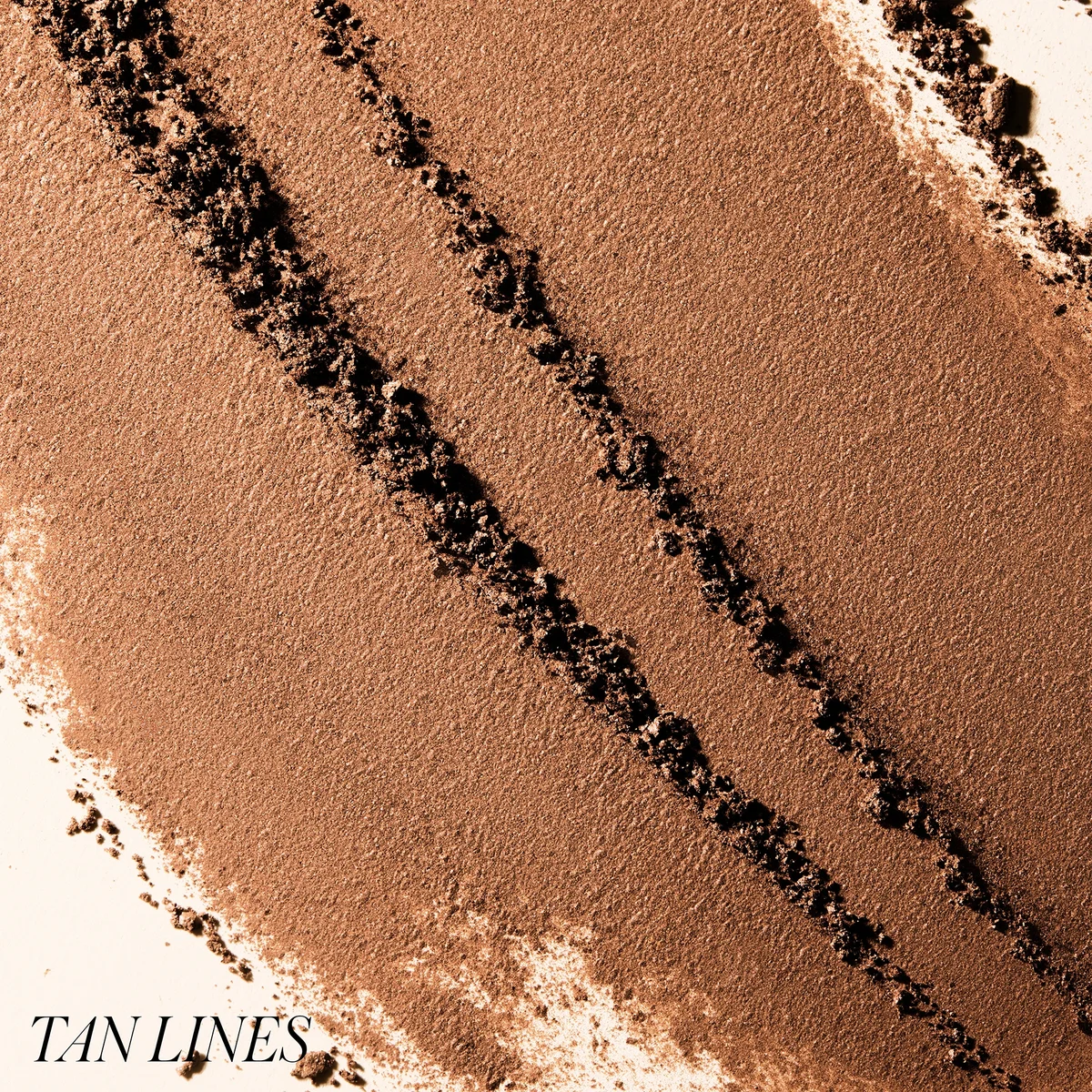 Close-up of tan makeup swatch with 'TAN LINES' text