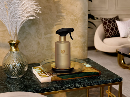 A bottle of Versace Armani styling spray with a black trigger sprayer and gold cap, displayed on a glass tray on a marble table in a luxury interior setting.