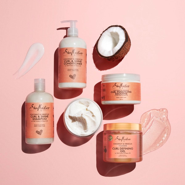 Set of hair care products including shampoo, conditioner, and masks on a pink background with a coconut half.