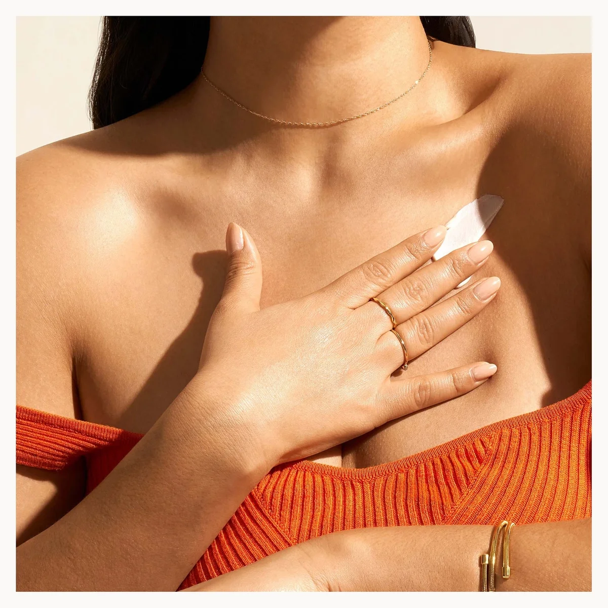 Person wearing an orange top with a close-up of their shoulder and hand.