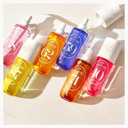 Five bottles of SK Innenseen sunscreen spray in different vibrant colors (pink, yellow, orange, blue, red) arranged diagonally on a light beige background with soft shadows.