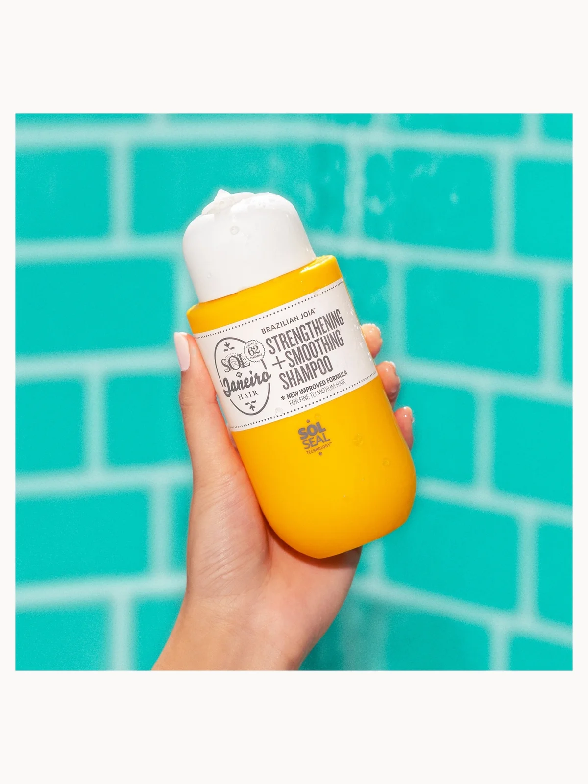 Hand holding a yellow shampoo bottle with a white label against a teal tiled background