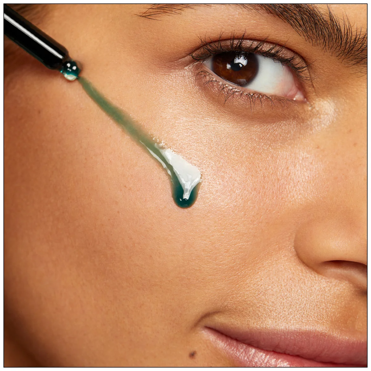 Close-up of a woman's face with a dropper applying a green substance to her skin.
