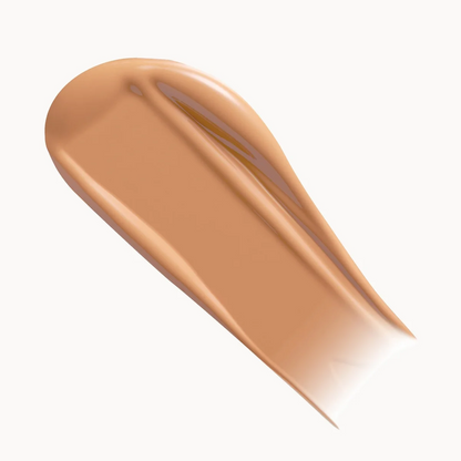 A smooth, glossy swatch of liquid foundation or concealer in a warm light tan shade, presented on a clean white background.