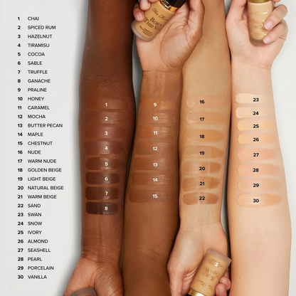A foundation shade swatch chart showing 30 different skin tone shades labeled with names like Chai, Spiced Rum, and Vanilla, alongside swatches applied to multiple arms and hands.