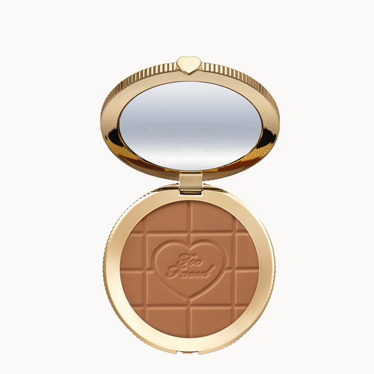 Too Loud bronzer compact in an open round gold case with a mirror, showing a warm medium-brown pressed powder with a heart-shaped embossing.