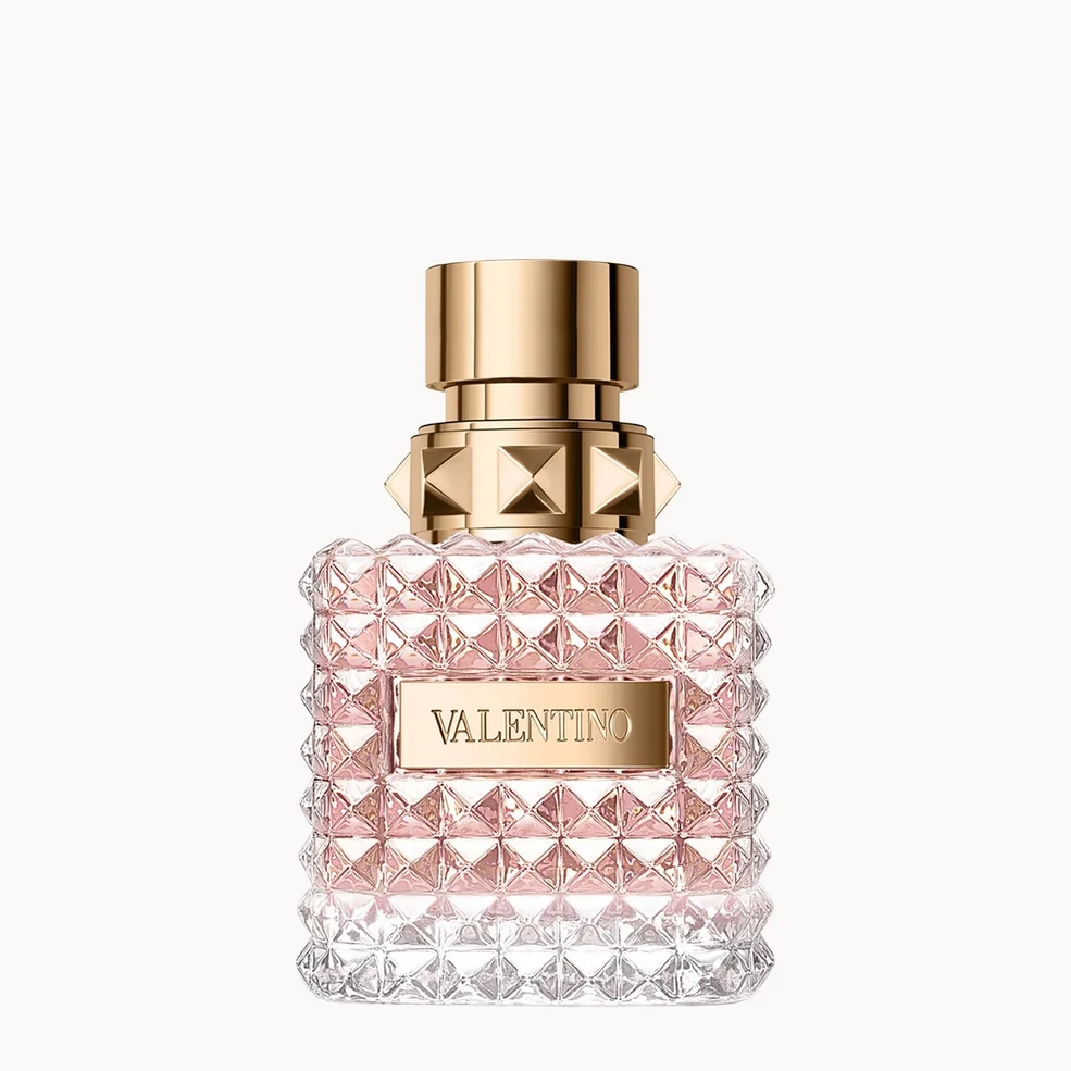 Valentino perfume bottle with a textured, faceted clear glass body showing pink liquid inside, topped with a gold cap and a gold brand plaque.