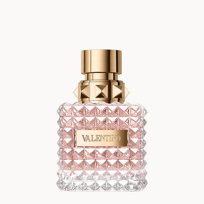 Valentino perfume bottle with a textured, faceted clear glass body showing pink liquid inside, topped with a gold cap and a gold brand plaque.
