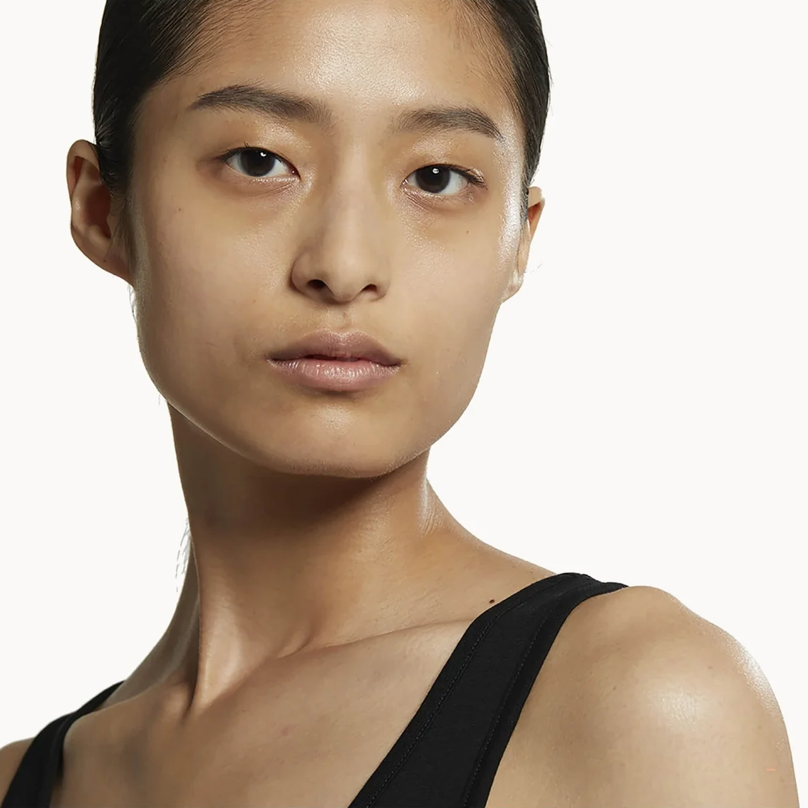 Close-up portrait of a model wearing a black strap top against a plain light background.