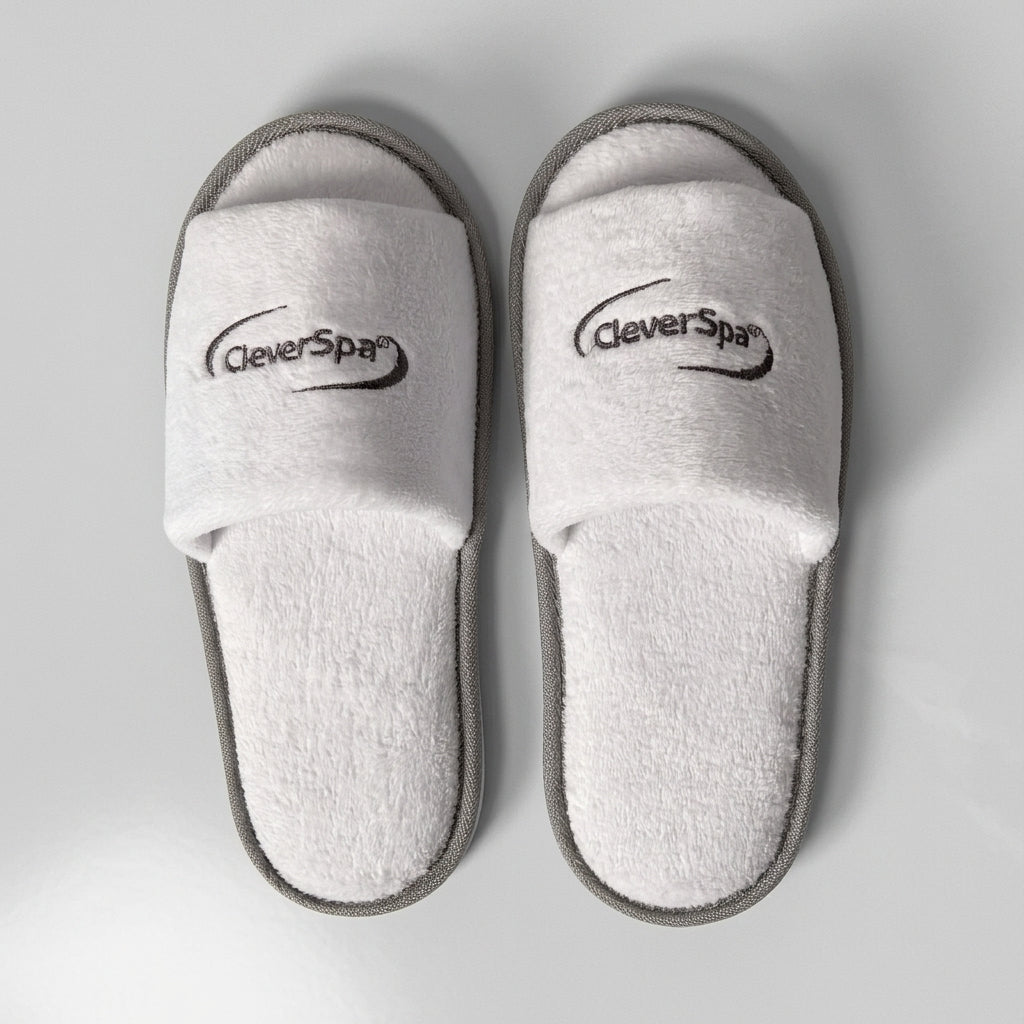 A pair of white terry cloth slide slippers with gray trim and the CleverPys brand logo printed on the straps, shown from a top-down view on a light gray background.