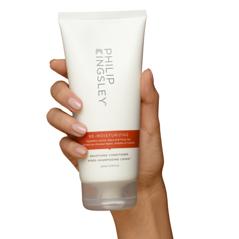 Hand holding a Philip Kingsley conditioner bottle on a white background