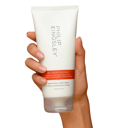 Hand holding a Philip Kingsley conditioner bottle on a white background